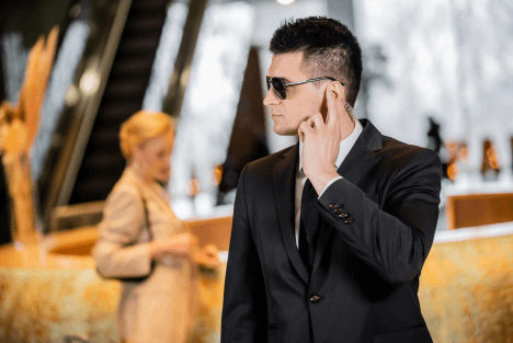Hotel security guard in a suit wearing an earpiece, standing near a lobby entrance and front desk