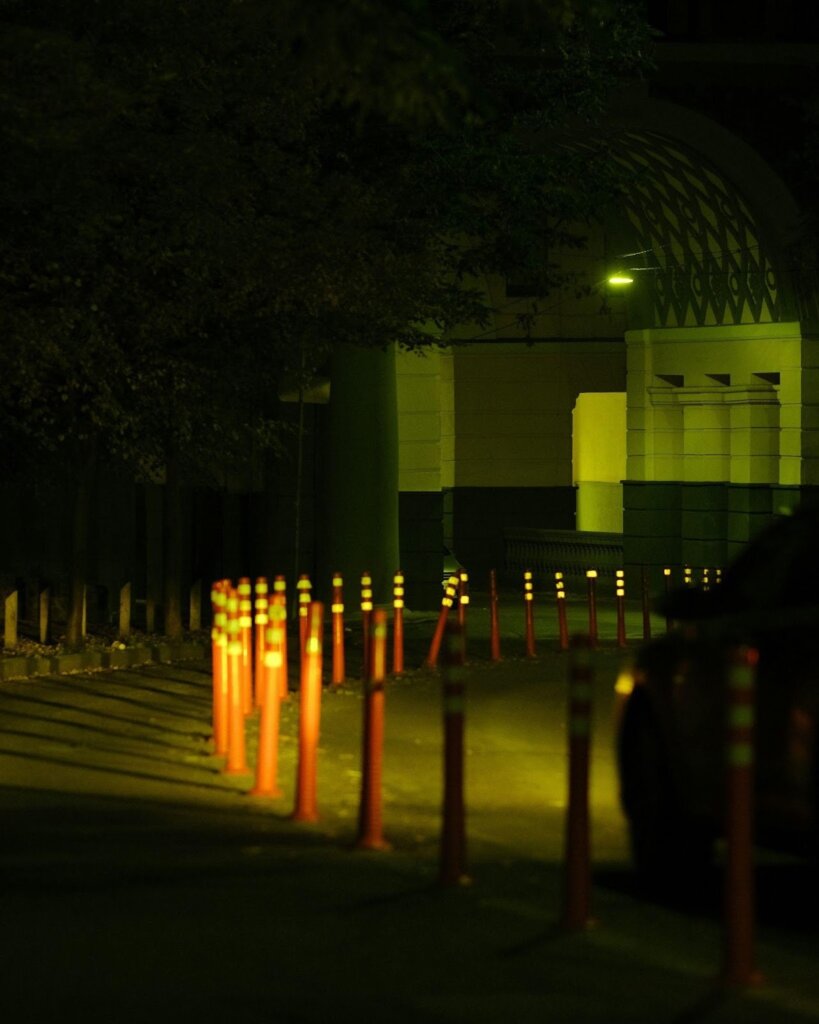 City street lights at night seen through a chain-link fence.