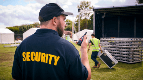 Event security staff coordinate via radio near an outdoor stage during a community festival.