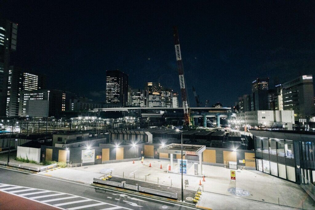 Night construction site with cranes and bright work lights illuminating the work area.