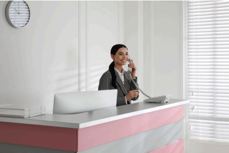 Reception desk staff member on the phone at an office counter, monitoring the entry area