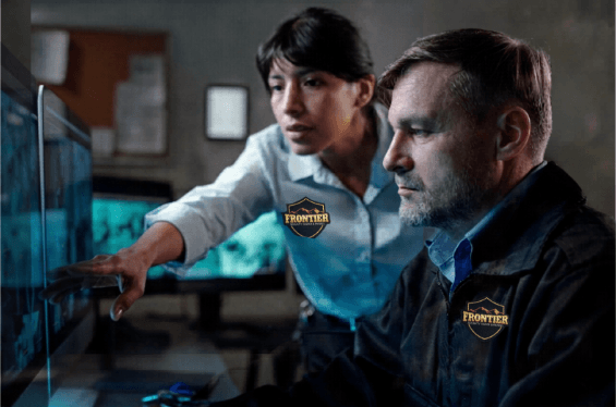 Security guard and colleague study surveillance footage on a computer screen, showing real-time review of camera feeds as part of a commercial security setup.