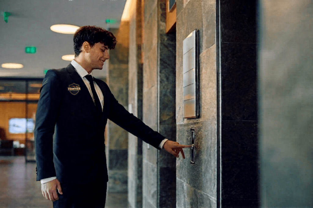 Hotel security guard in a suit presses an elevator button in a hallway, suggesting guest floor or common area patrol.