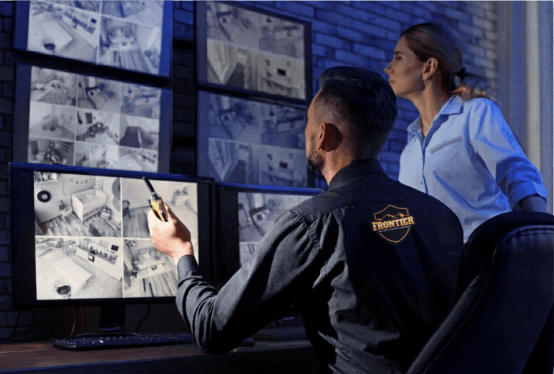 Two security staff watch a wall of surveillance monitors displaying multiple camera views, illustrating camera-based monitoring for business security.