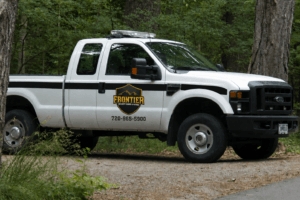 White Frontier service truck parked on a dirt road in a forest setting.